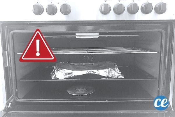 un plat à gratin recouvert de papier d'alu dans un four avec un panneau danger