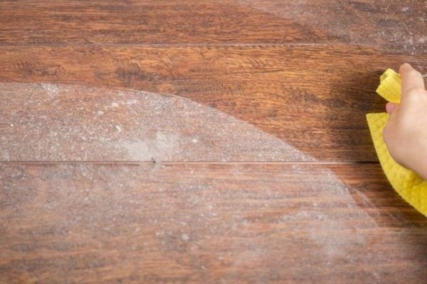 une table pleine de poussières avec une personne qui passe un chiffon jaune