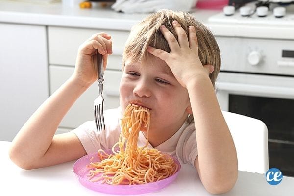 un enfant blond mange des spaghettis plein la bouche dans une assiette rose