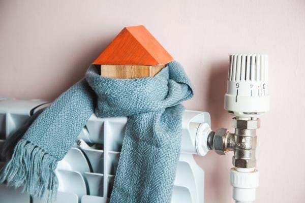 Un radiateur et une mini maison entouré d'une écharpe pour économiser du chauffage