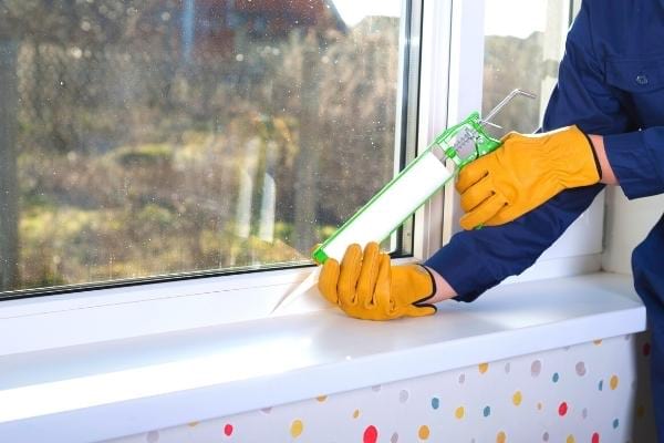 Du mastic appliqué sur les bords d'une fenêtre pour éviter la condensation