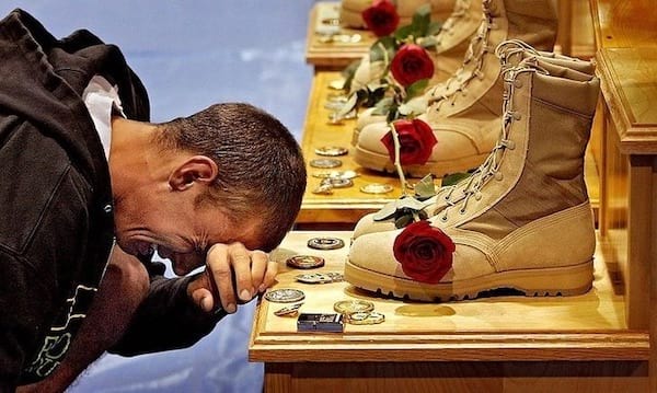 Un homme pleurant devant des chaussures de militaires