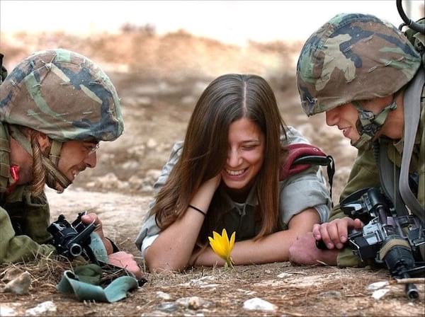 Deux militaires avec une femme au milieu souriant devant une fleur jaune