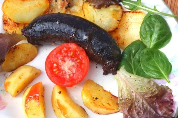 une assiette avec du boudin, des pommes de terre , de la salade et des tomates