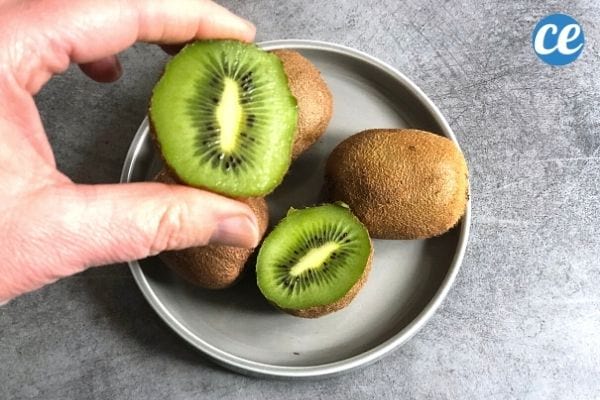deux kiwis dans une assiette grise et un kiwi coupé en deux tenu dans une main