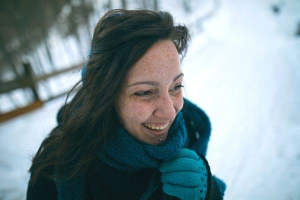 une femme souriante avec une écharpe et des gants bleus dans un paysage enneigé