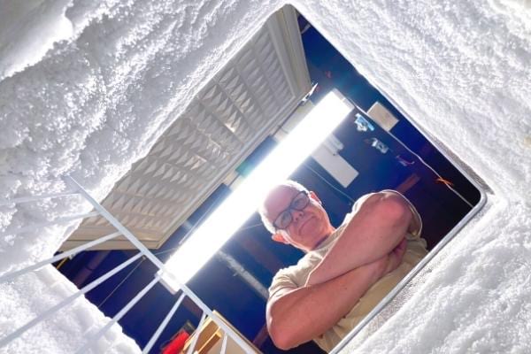 Un homme qui regarde son congélateur plein de givre qui consomme beaucoup d'électricité