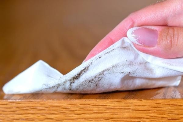 Une femme qui dépoussière un meuble en bois avec un tissu et de l'huile d'olive