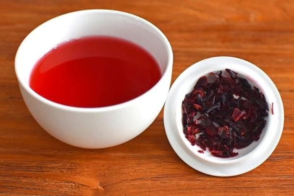 Eine weiße Tasse mit Bissap mit Hibiskusblüten in der Nähe