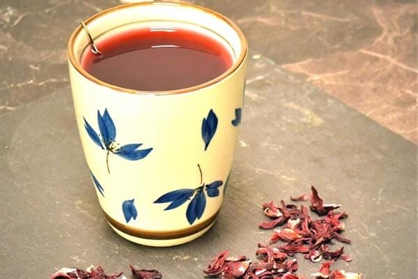Weiße Tasse mit blauen Blüten, die Bissap aus Hibiskusblüten enthält