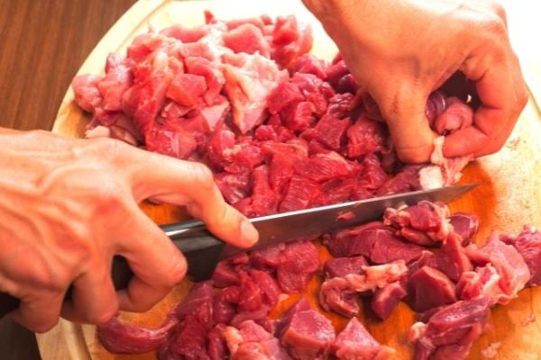 Un homme avec un couteau qui coupe de la viande rouge riche en cholestérol