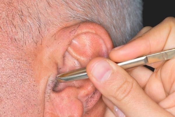 A man having his ear hair removed with tweezers