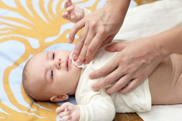 a woman cleans the baby's mouth with a cotton ball