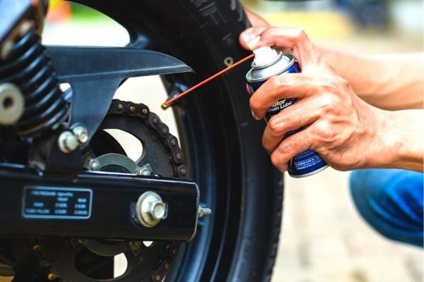 Un homme qui lubrifie une chaine de moto pour consommer moins d'essence