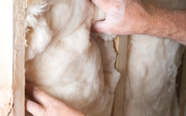 Un homme qui isole son logement avec de la laine de verre pour consommer moins de bois de chauffage