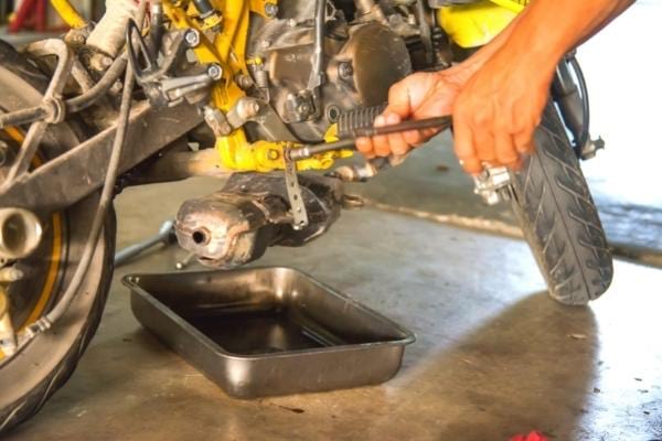 Un homme faisant la vidange de sa moto pour consommer moins d'essence
