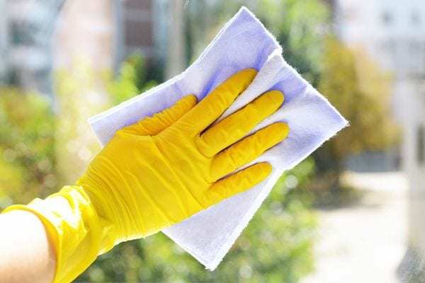Une personne lavant une fenêtre avec des gants jaunes et un chiffon violet 