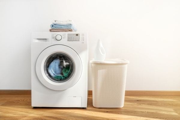 une machine à laver avec du linge dedans et dessus à côté d'une panière à linge