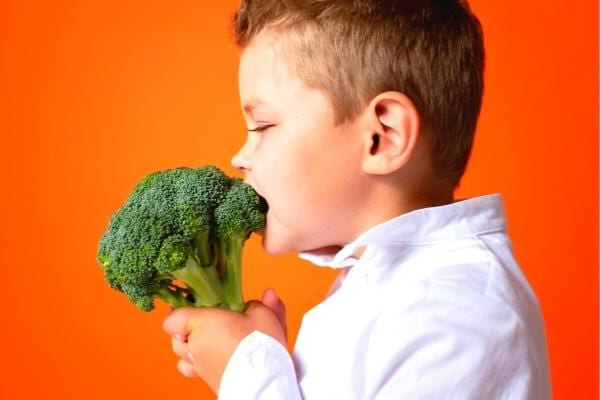 Un enfant qui croque un brocoli plein de vitamine C