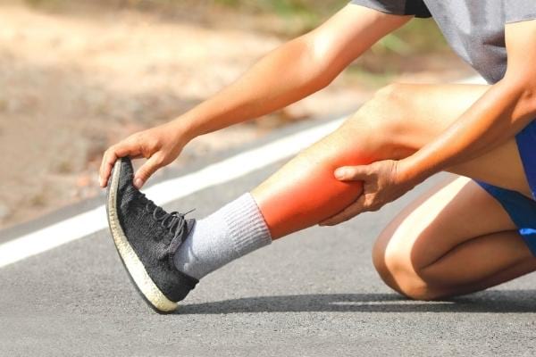 Un homme qui s'étire la jambe suite à des courbatures qu'il peut soulager avec l'huile d'amande douce