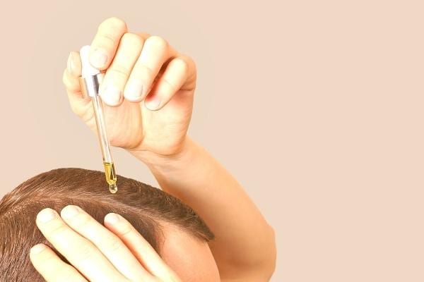 Une main qui tient une pipette remplie d'huile d'amande douce pour le cuir chevelu