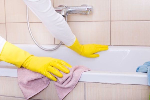 Une personne nettoyant une baignoire avec un chiffon micro-fibres rose 
