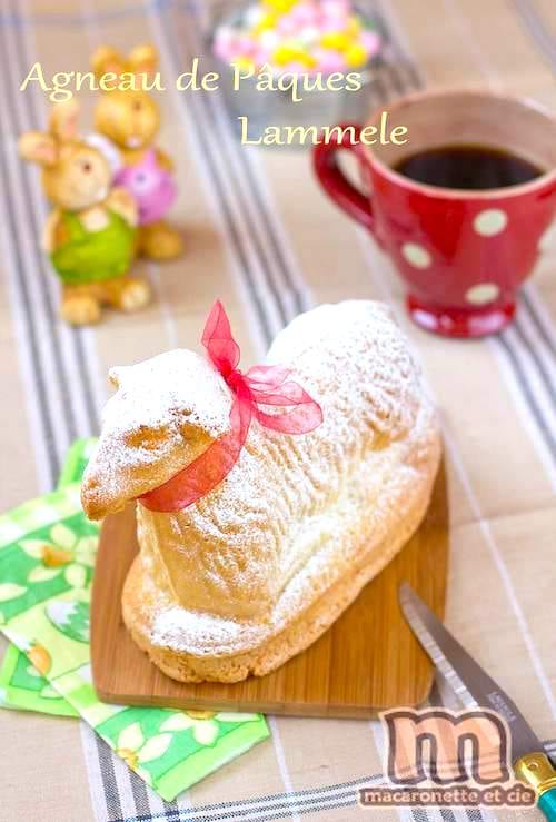 An Easter lamb cake with a red ribbon a red cup with a white dot and bunny figurines