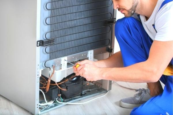 Un homme replace le bac de récupération d'un frigo pour qu'il ne fasse plus de bruit