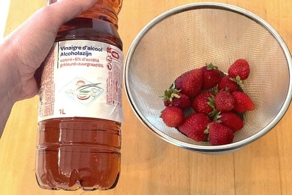 des fraises dans une passoire et du vinaigre d'alcool colore pour les désinfecter