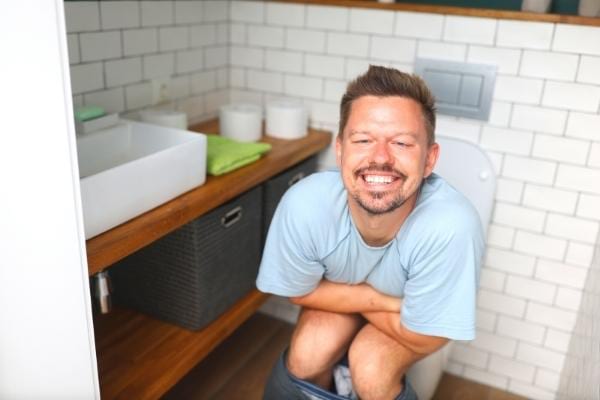 Un homme assis sur des toilettes qui sourit