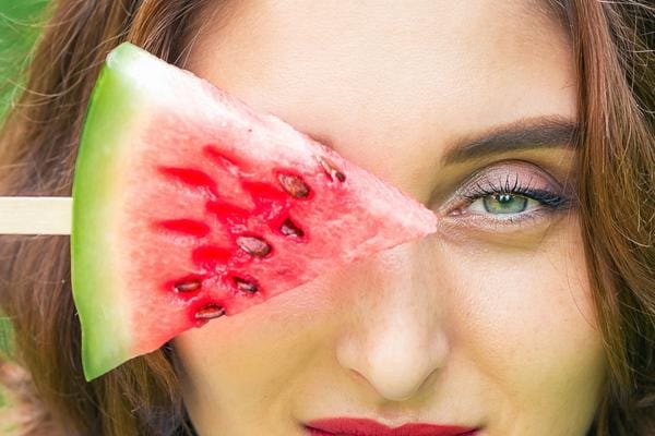 Un morceau de pastèque sur un bâton devant l'oeil d'une femme