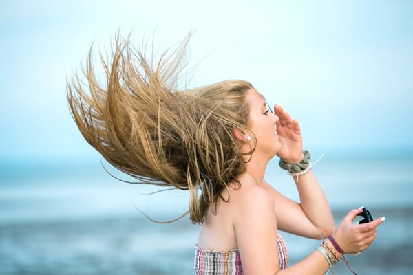 fille blonde qui fait voler ses cheveux sur la plage astuce pour les entretenir en vacances