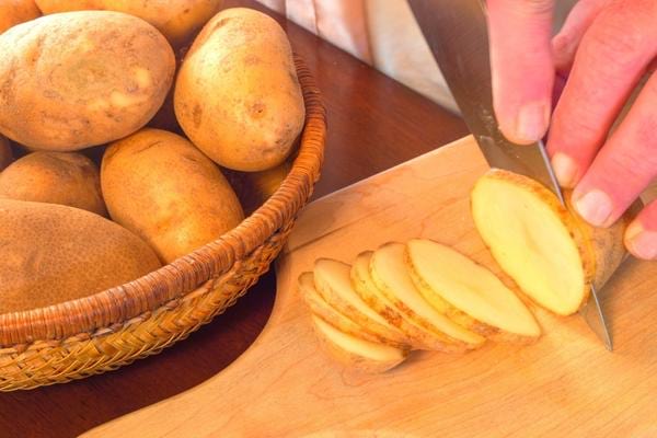 un homme qui coupe des pommes de terre pour faire un cataplasme qui soulage les douleurs au talon