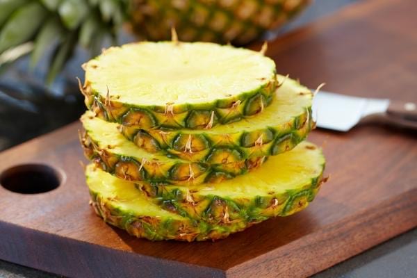 Cinq lamelles d'ananas sur une planche à découper 