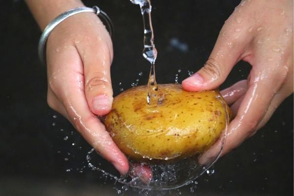 Une personne qui lave une pomme de terre à l'eau