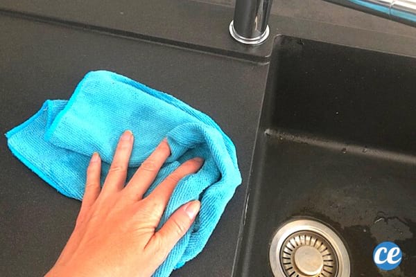 main qui essuie un évier noir avec un chiffon bleu
