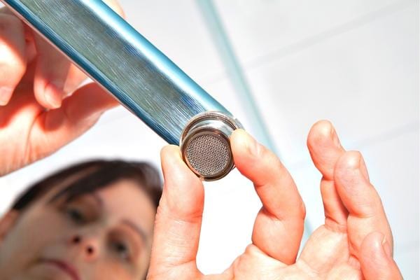 Une femme qui installe un mousseur de robinet pour économiser de l'eau