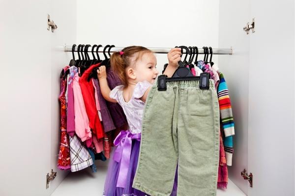 Une petite fille tenant un pantalon dans un dressing