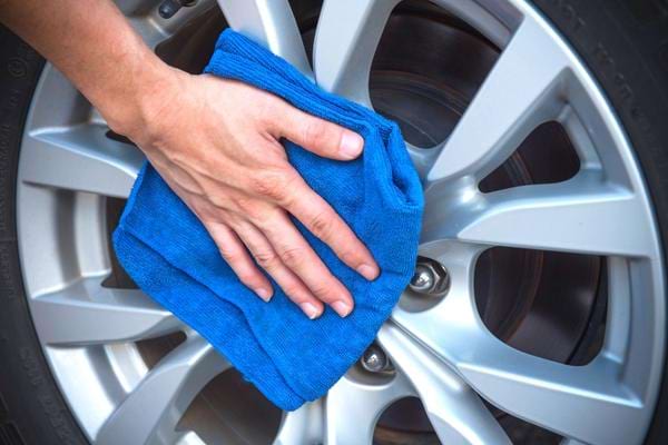 Une personne nettoyant une jante de voiture avec un chiffon micro-fibre bleu