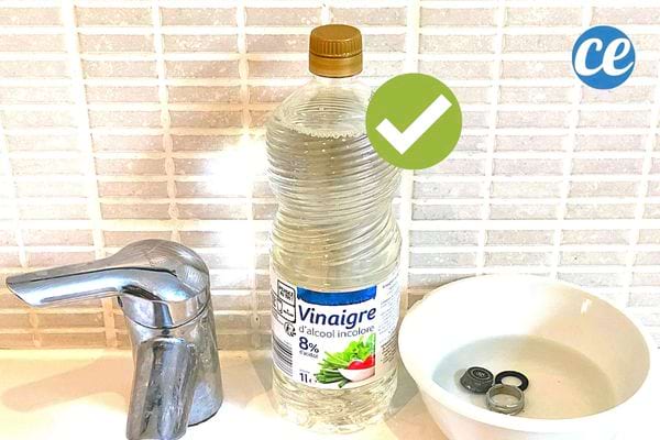 une bouteille de vinaigre blanc sur un lavabo à côté d'un bol contenant un mousseur et du vinaigre