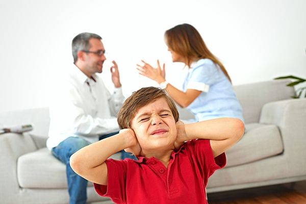 un homme et une femme se disputent sur un canapé devant un enfant qui se bouche les oreilles