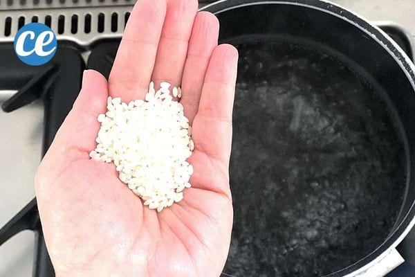 une poignée de riz dans une main au-dessus d'une casserole d'eau bouillante
