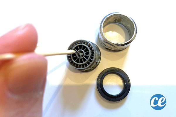 Une personne enlève les dépôts de calcaire sur un mousseur avec un cure-dent