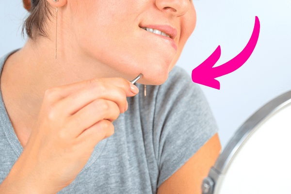 Une femme qui s'épile à la pince à épiler pour se débarrasser des poils au menton