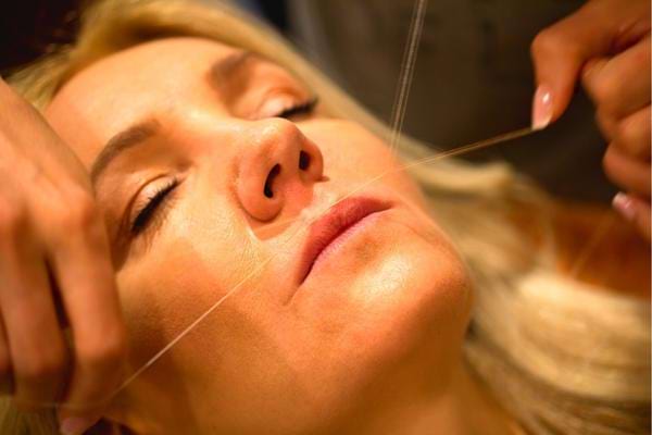 Une femme qui s'épile au fil pour se débarrasser des poils au menton