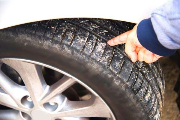 Un homme montrant du doigt l'usure d'un pneu pour prolonger sa durée de vie