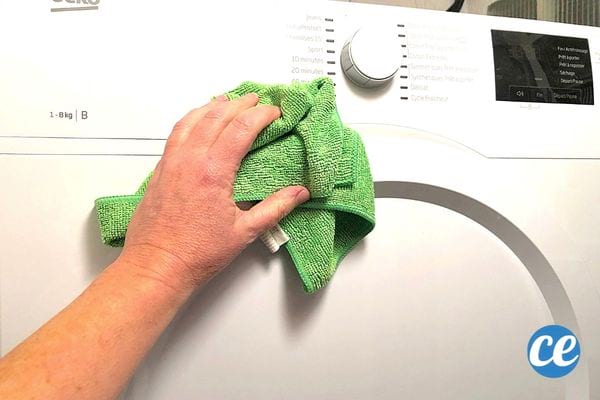 A person cleaning the front of their dryer with a green microfiber cloth 