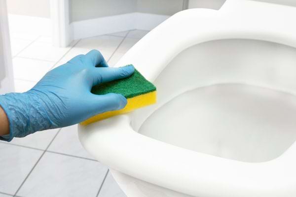 Une personne nettoyant une cuvette de toilette avec une éponge