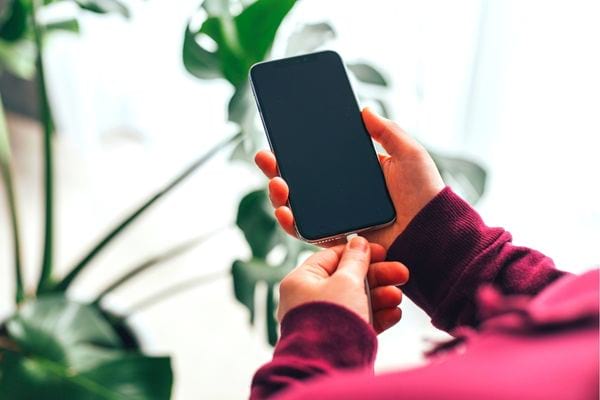 Une personne vêtu d'un pull couleur bordeaux avec un téléphone qui charge dans ses mains