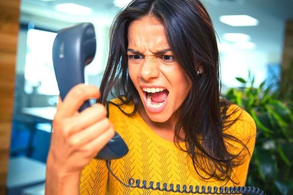 Une femme avec un pull jaune en colère avec le téléphone